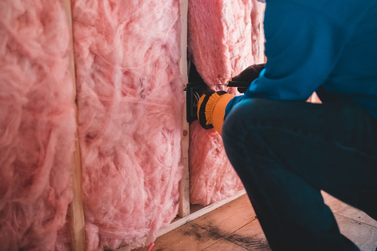 Handwerker verlegt Mineralwolle-Dämmung zwischen Holzständern in einer Wand
