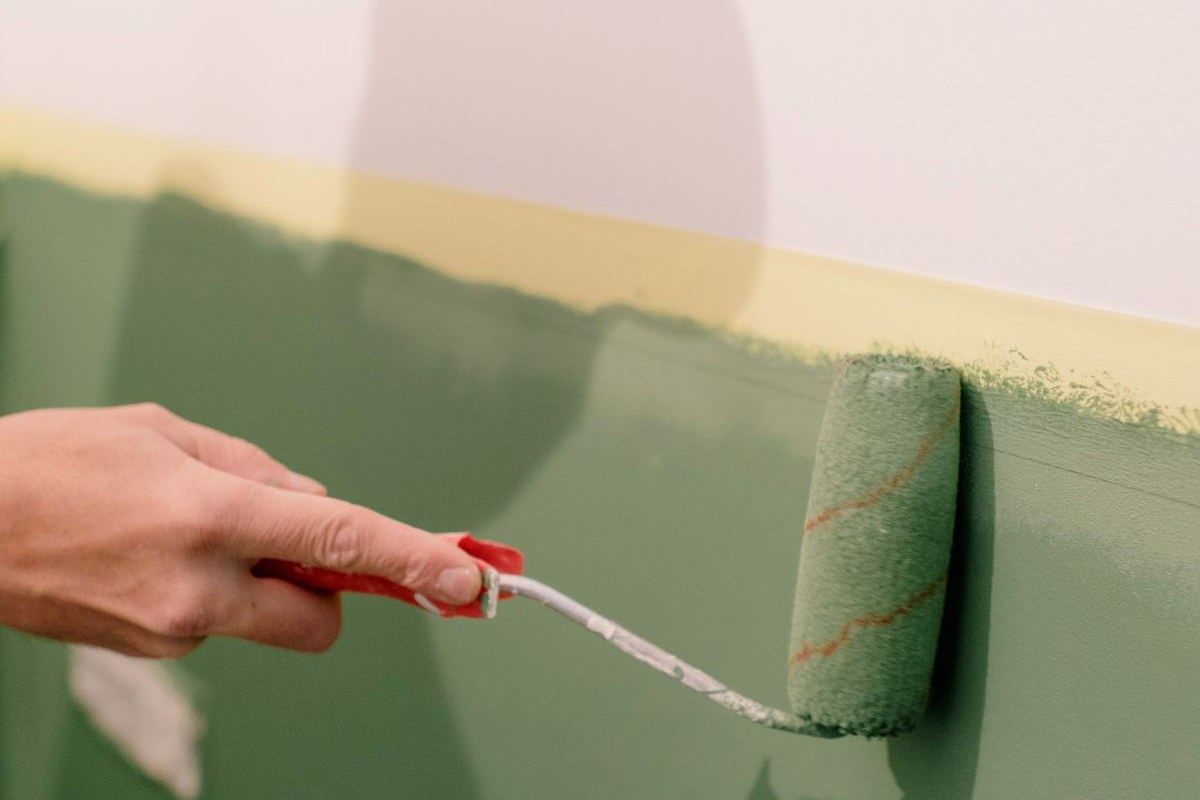 Hand streicht eine Wand mit Farbroller grün